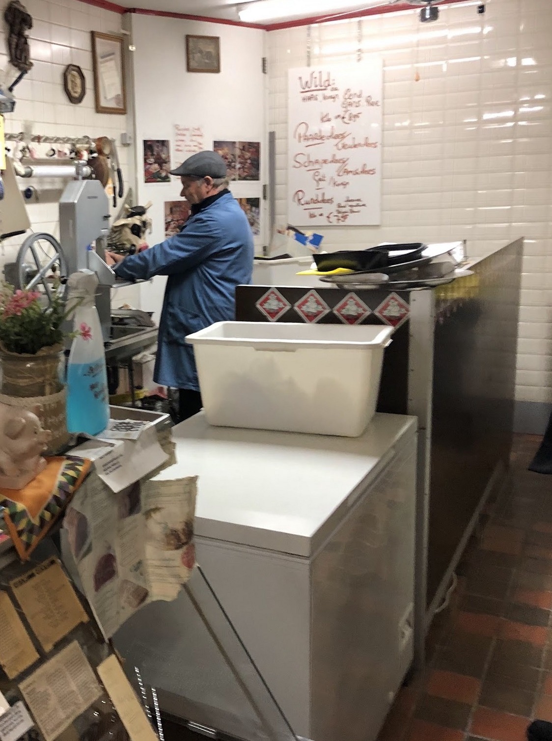 De slager aan de snijmachine in de winkel, met het handgeschreven wildbord aan de muur